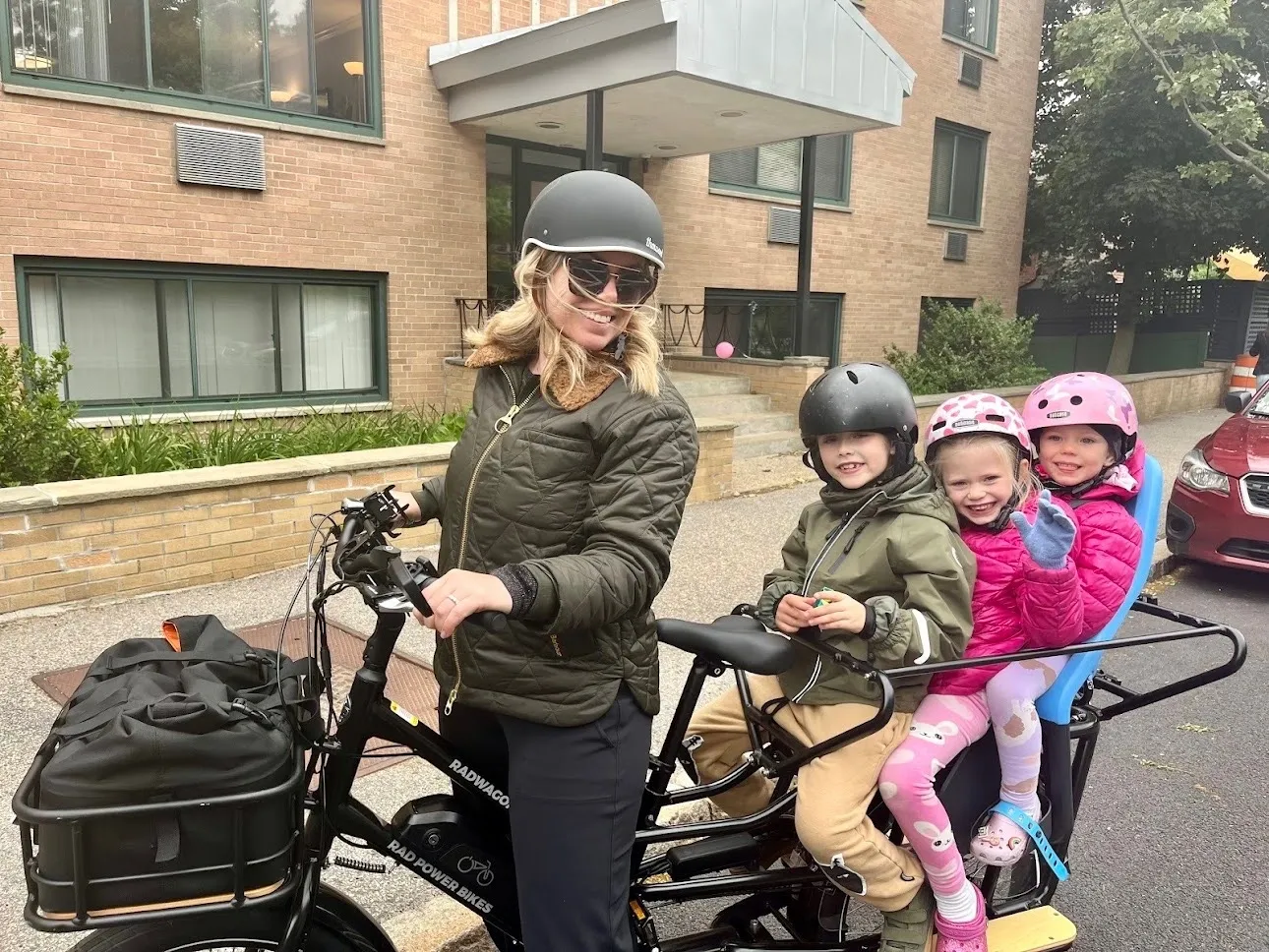 A parent with two children riding in the back of a cargo e-bike